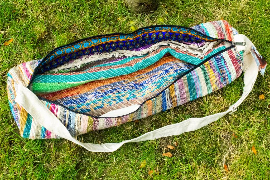 Recycled sari yoga mat bag in vibrant colors hanging on wall next to rolled JadeYoga mat and wet pocket open