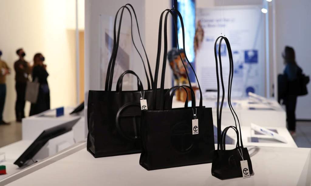 Side-by-side comparison of real versus fake hardware on a Telfar Clemens tote bag, showing engraved zipper details and weight differences.
